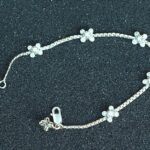 Pulsera fina en oro blanco 18K con cinco flores formadas por diamantes brillantes, distribuidas a lo largo de la cadena